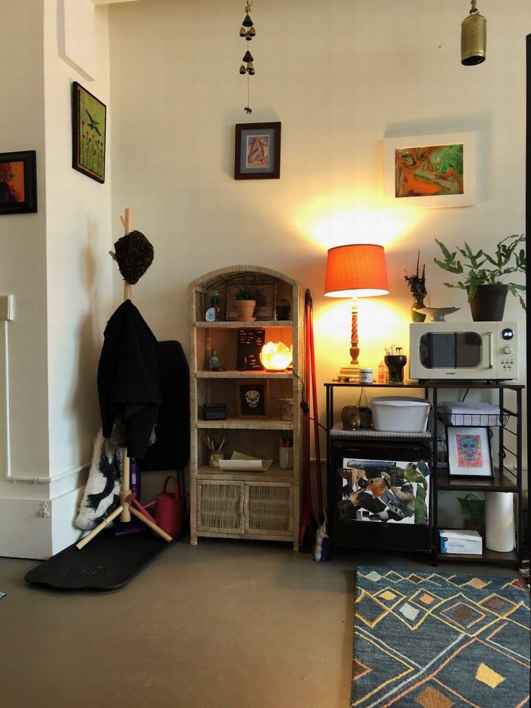 Entry corner with a coat hook, a small bookshelf, a warm lamp and a microwave cart