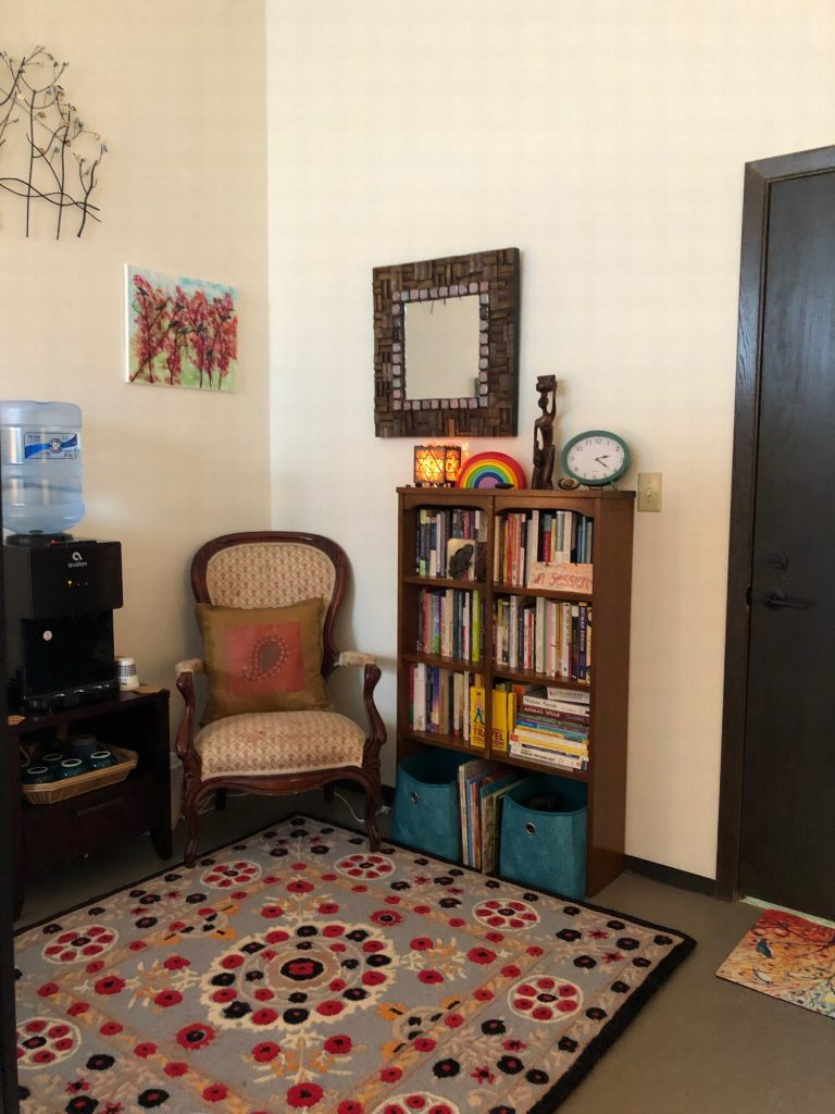 An armchair beside a bookcase and water cooler, with a small rainbow on the shelf