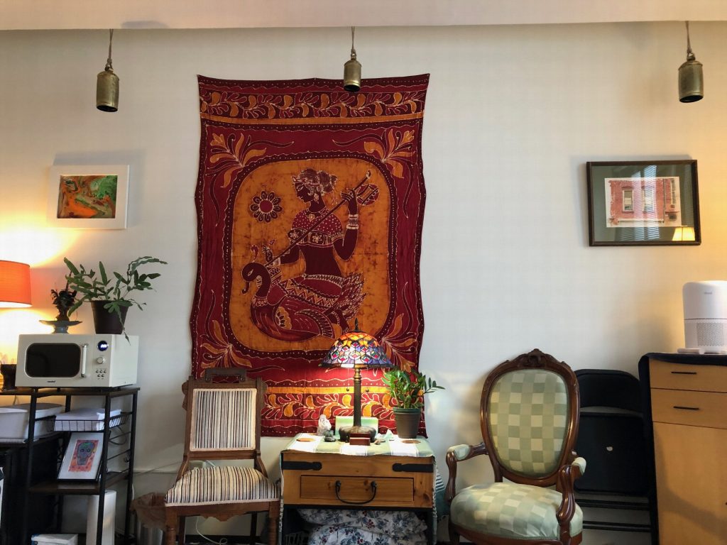 A red tapestry above a small table and stained-glass lamp, between two armchairs