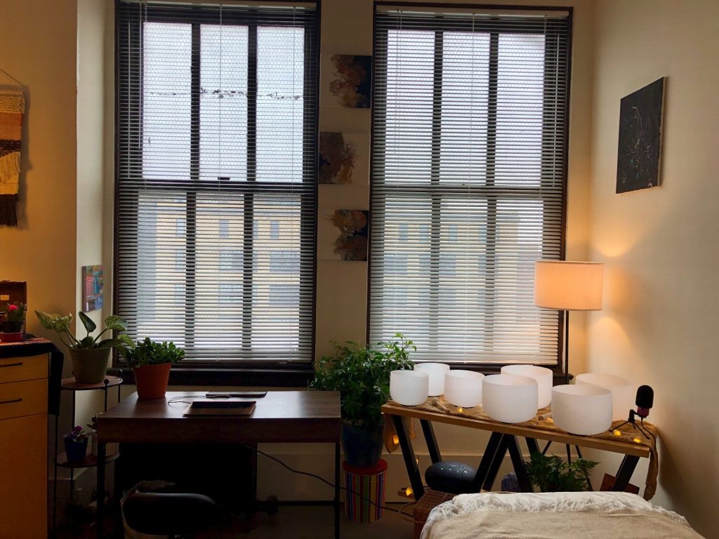 Crystal singing bowls on a low table beneath the windows, beside a lamp and plants