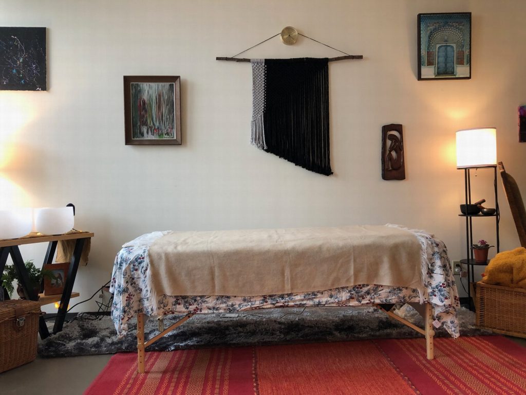 The bodywork table on a red rug, beneath a black macramé wall hanging